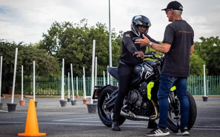 Instructor standing beside a rider on a training motorcycle at a manoeuvre yard
